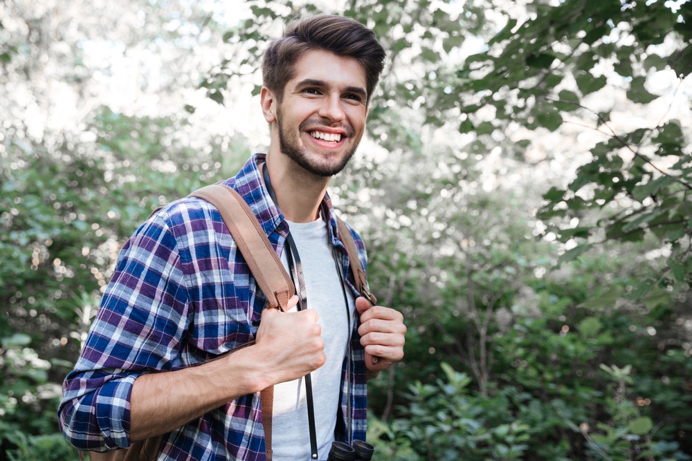 Side,View,Of,Smiling,Man,With,Backpack,In,Forest.,Holds